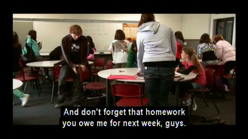 Students at circular tables in a classroom setting. Caption. And don't forget that homework you owe me for the next week, guys.
